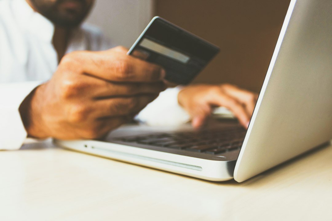 A person holding a payment card beside a laptop, illustrating an online transaction record check.