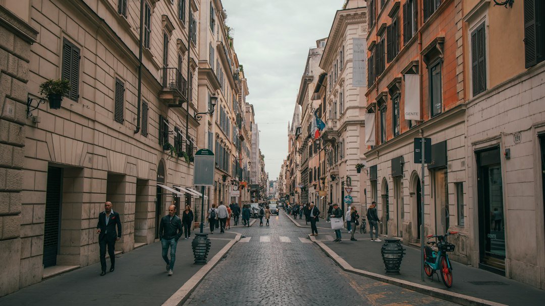 Pedestrians on a city street with stone buildings